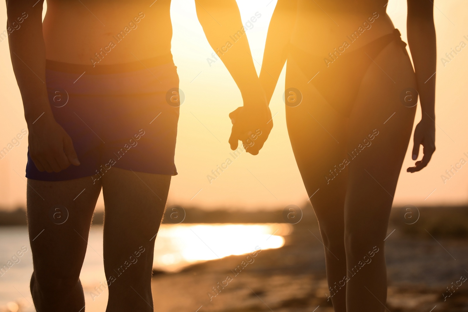 Photo of Woman in bikini holding hands with her boyfriend on beach at sunset, closeup. Lovely couple