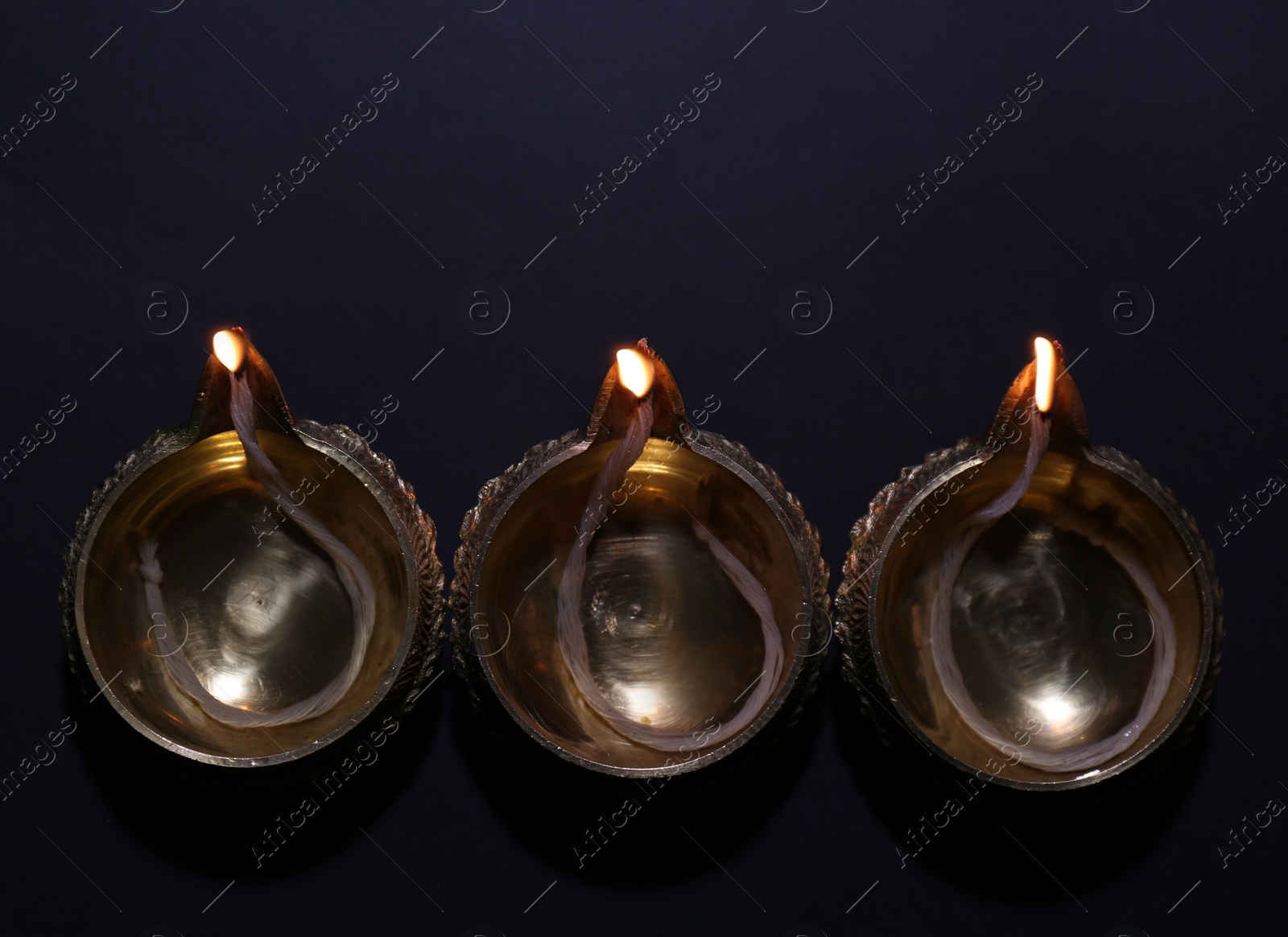 Photo of Lit diyas on dark background, flat lay. Diwali lamps