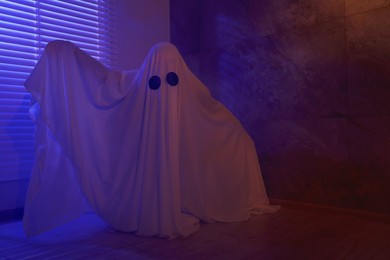 Creepy ghost. Woman covered with sheet near window in color lights