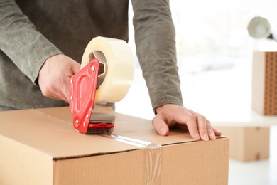 Photo of Young man packing moving box indoors, closeup