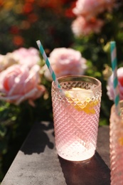 Photo of Glass of pink rose lemonade on table in blooming garden