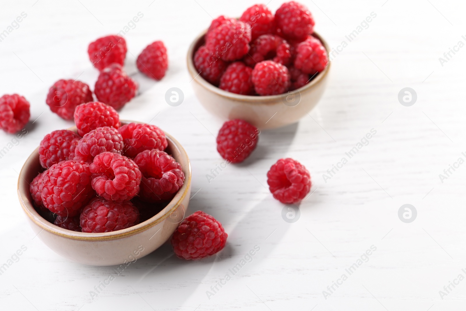 Photo of Tasty ripe raspberries on white wooden table, space for text