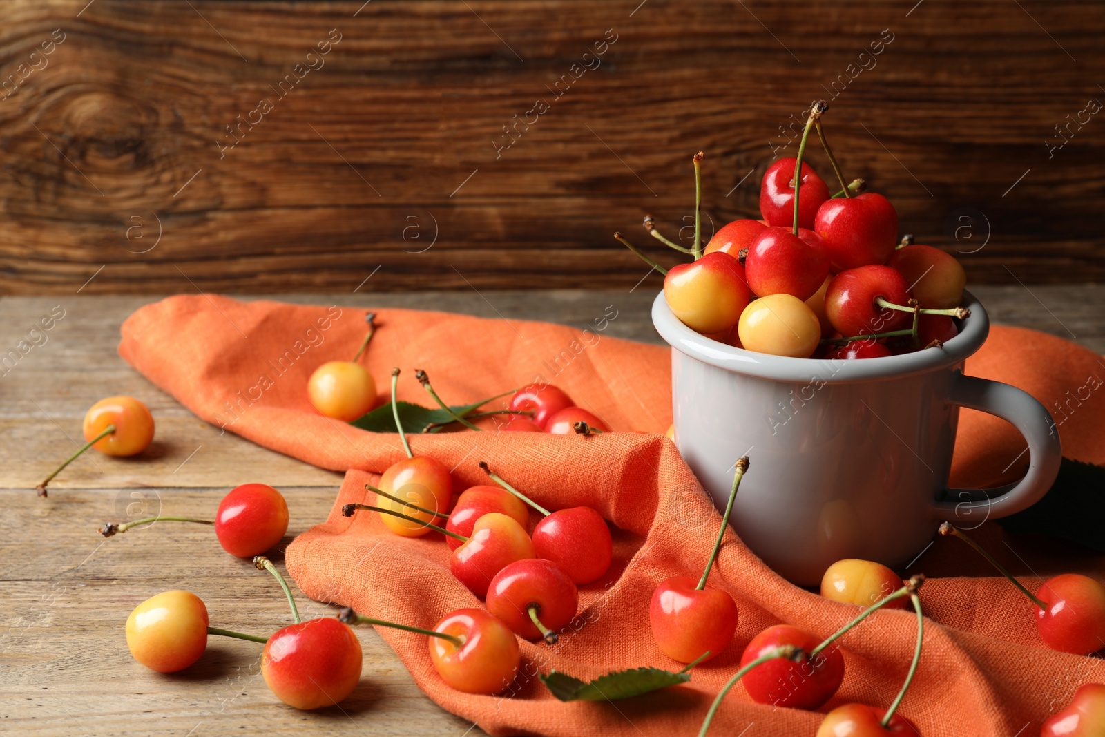 Photo of Sweet red cherries in mug on wooden table, space for text