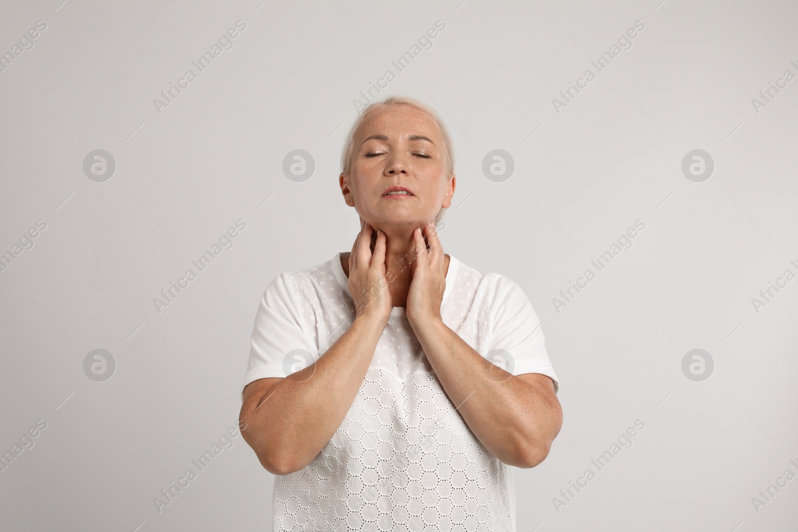 Photo of Mature woman doing thyroid self examination on light grey background