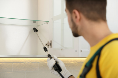 Photo of Pest control worker spraying insecticide on furniture in kitchen, closeup