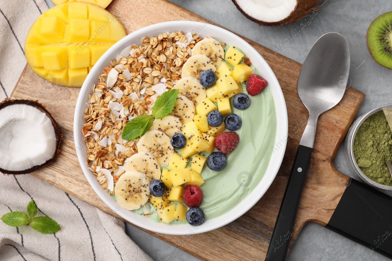 Photo of Tasty matcha smoothie bowl with fresh fruits and oatmeal served on grey table, flat lay. Healthy breakfast