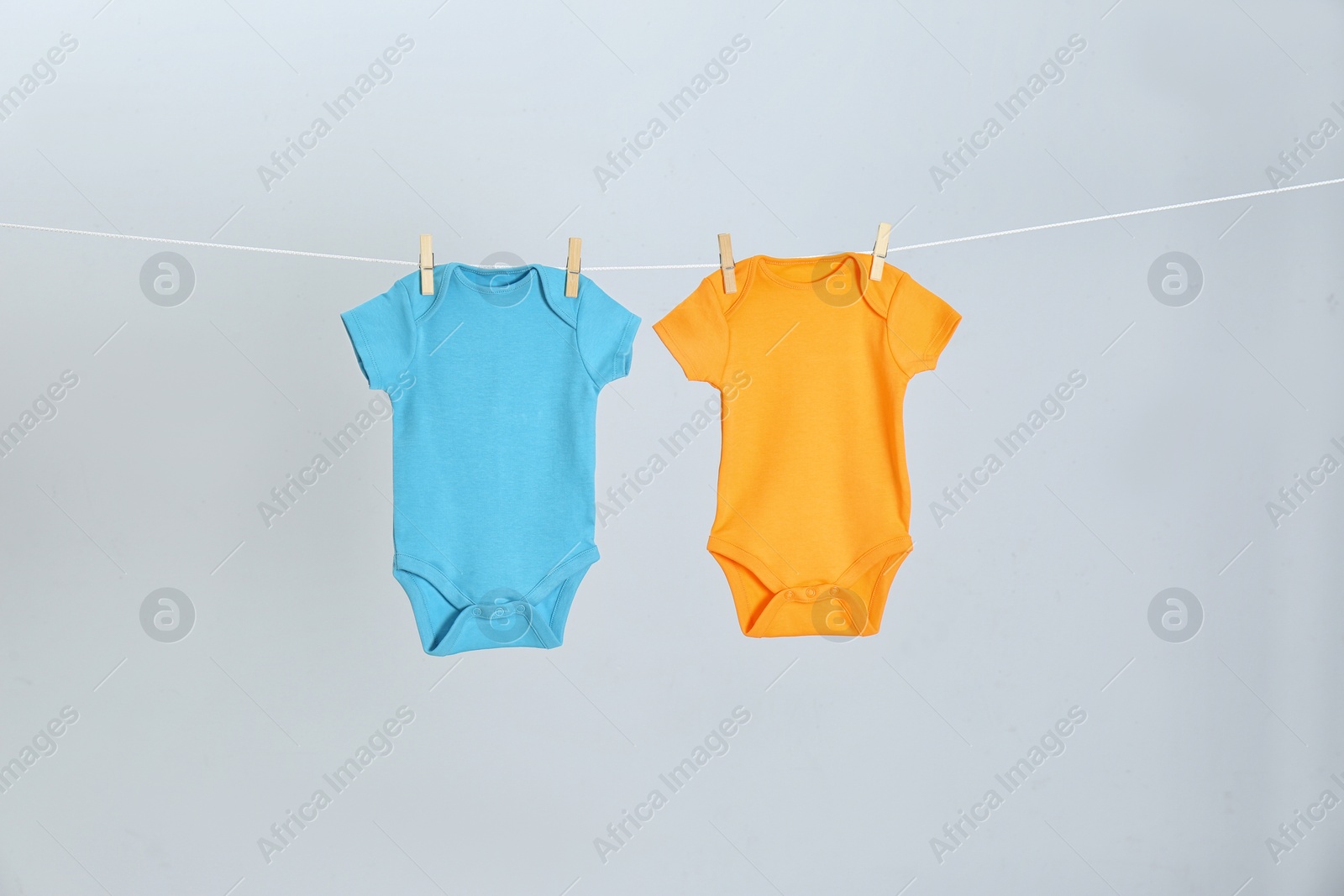 Photo of Different baby onesies hanging on clothes line against light grey background. Laundry day