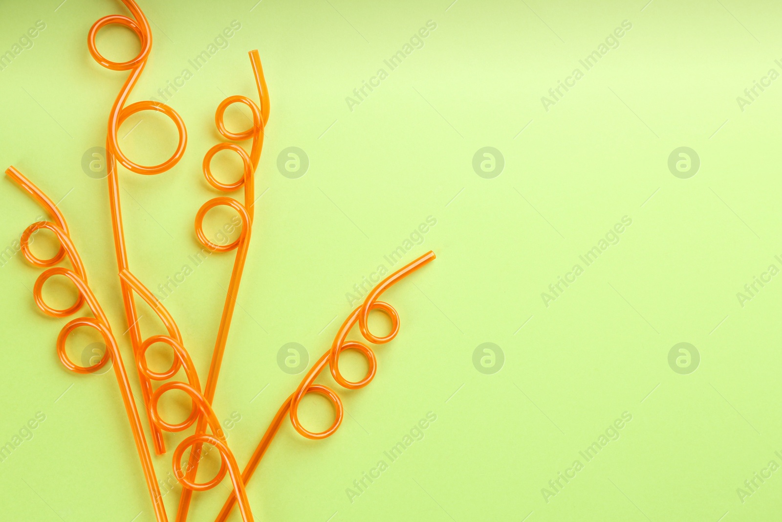 Photo of Orange plastic drinking straws on green background, flat lay. Space for text