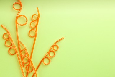 Photo of Orange plastic drinking straws on green background, flat lay. Space for text