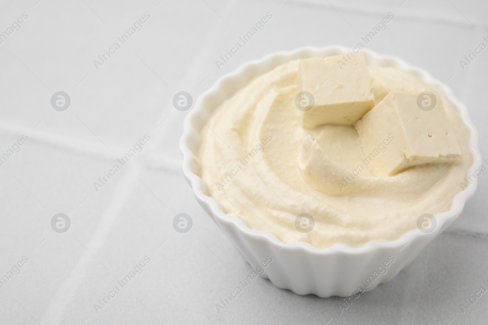 Photo of Delicious tofu sauce in bowl on white tiled table, closeup. Space for text