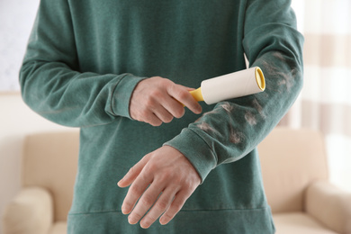 Man removing hair from green sweatshirt with lint roller on light background, closeup