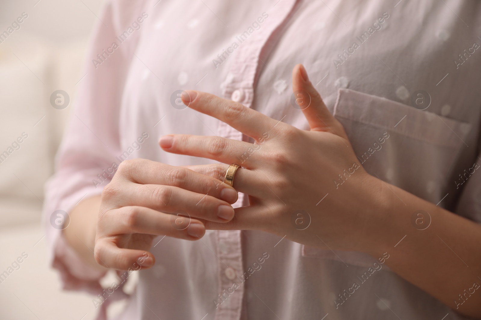 Photo of Woman taking off wedding ring indoors, closeup. Divorce concept