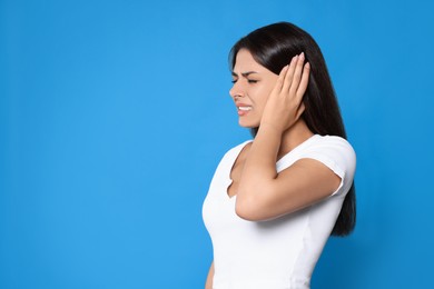 Young woman suffering from ear pain on light blue background, space for text