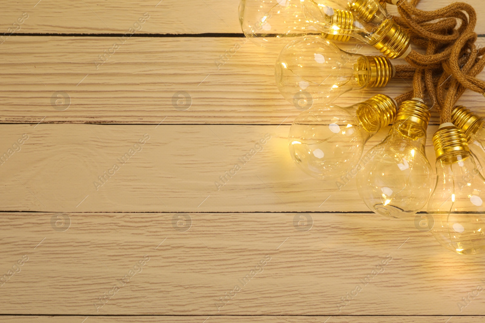 Photo of String lights with lamp bulbs on wooden background, top view. Space for text