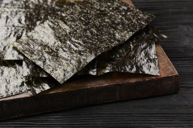 Photo of Wooden board with dry nori sheets on black table, closeup