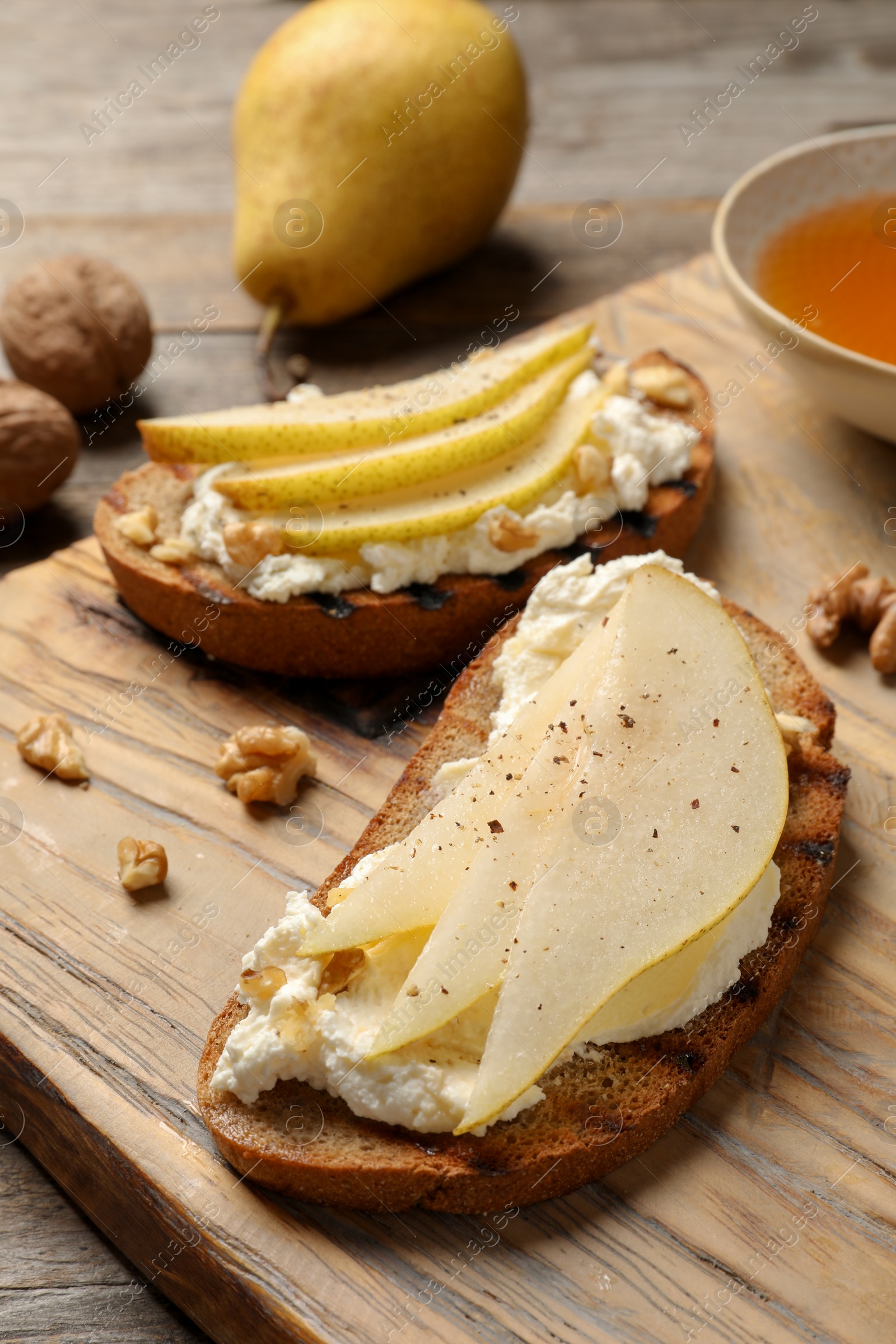 Photo of Toasted bread with tasty cream cheese and pear on wooden board