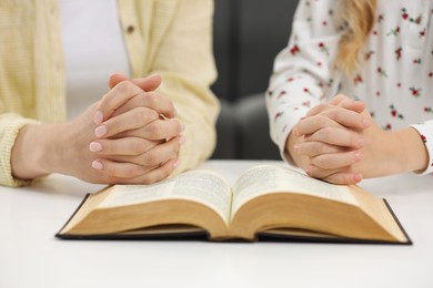 Girl and her godparent praying over Bible together at table indoors, closeup