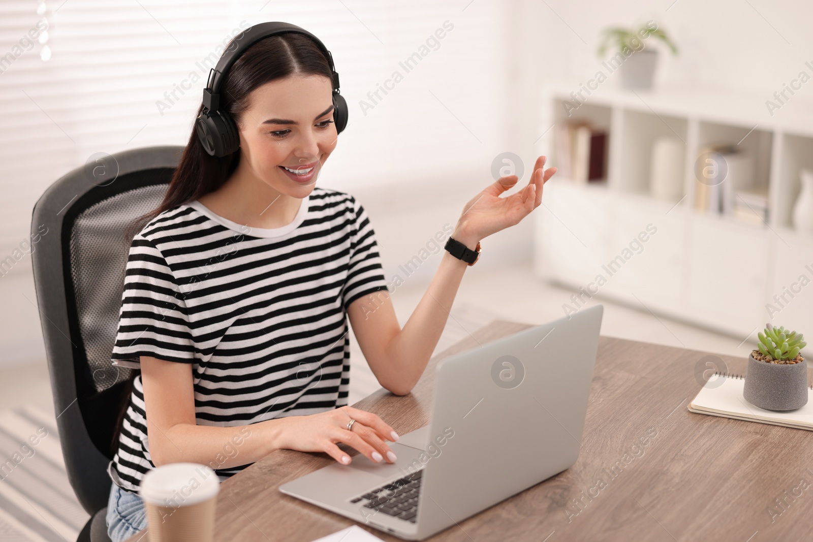 Photo of Young woman in headphones using video chat during webinar at table in room