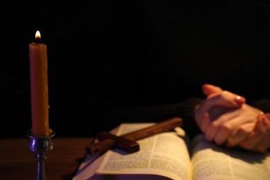 Photo of Woman praying at table with burning candle and Bible, closeup