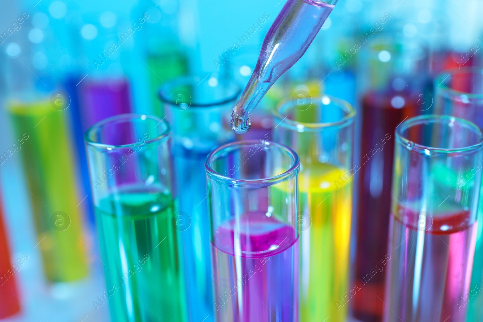 Photo of Dripping liquid from pipette into test tube on light blue background, closeup