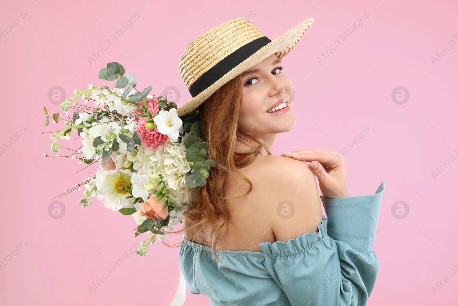 Photo of Beautiful woman in straw hat with bouquet of flowers on pink background