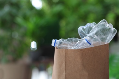 Photo of Used plastic bottles in paper bag on blurred background, space for text. Recycling problem