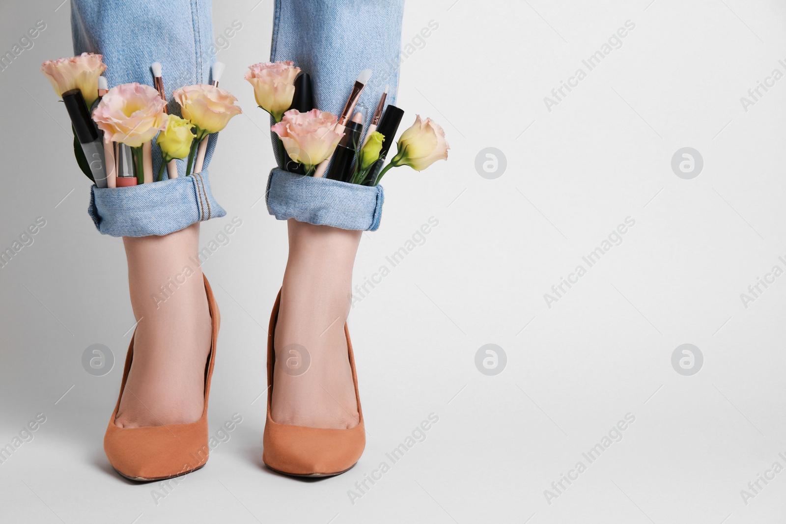 Photo of Woman in stylish jeans with roses and cosmetics on white background, closeup. Space for text