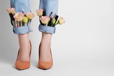 Photo of Woman in stylish jeans with roses and cosmetics on white background, closeup. Space for text