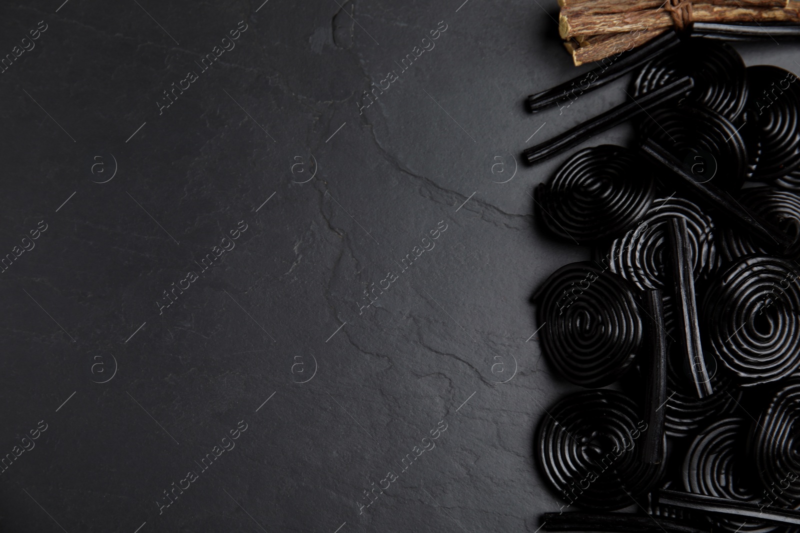 Photo of Tasty candies and dried sticks of liquorice root on black table, flat lay. Space for text