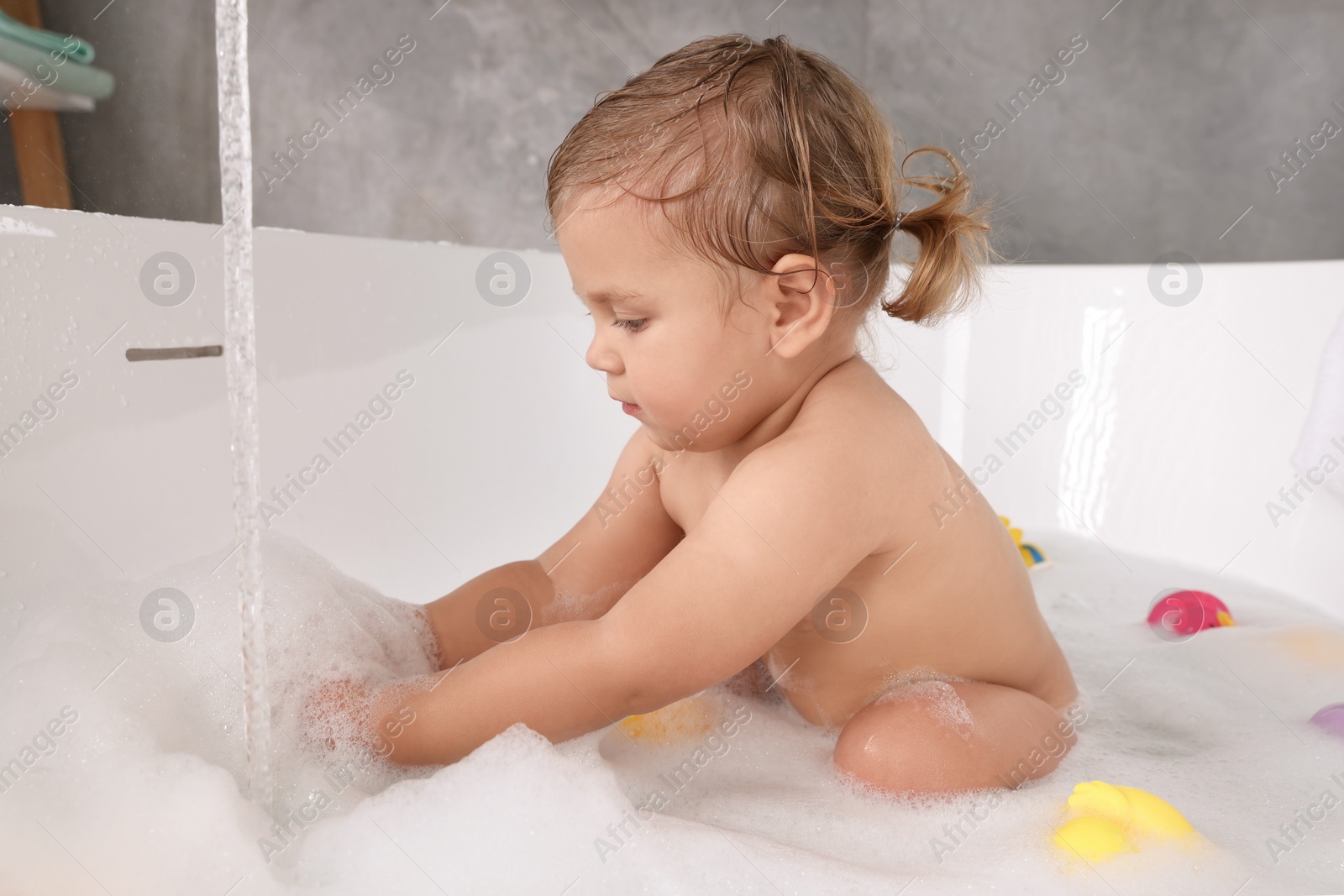 Photo of Cute little girl taking bubble bath with toys indoors