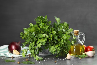 Fresh parsley, oil and other products on grey table