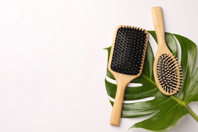 Photo of Wooden hairbrushes and green leaf on white background, flat lay. Space for text