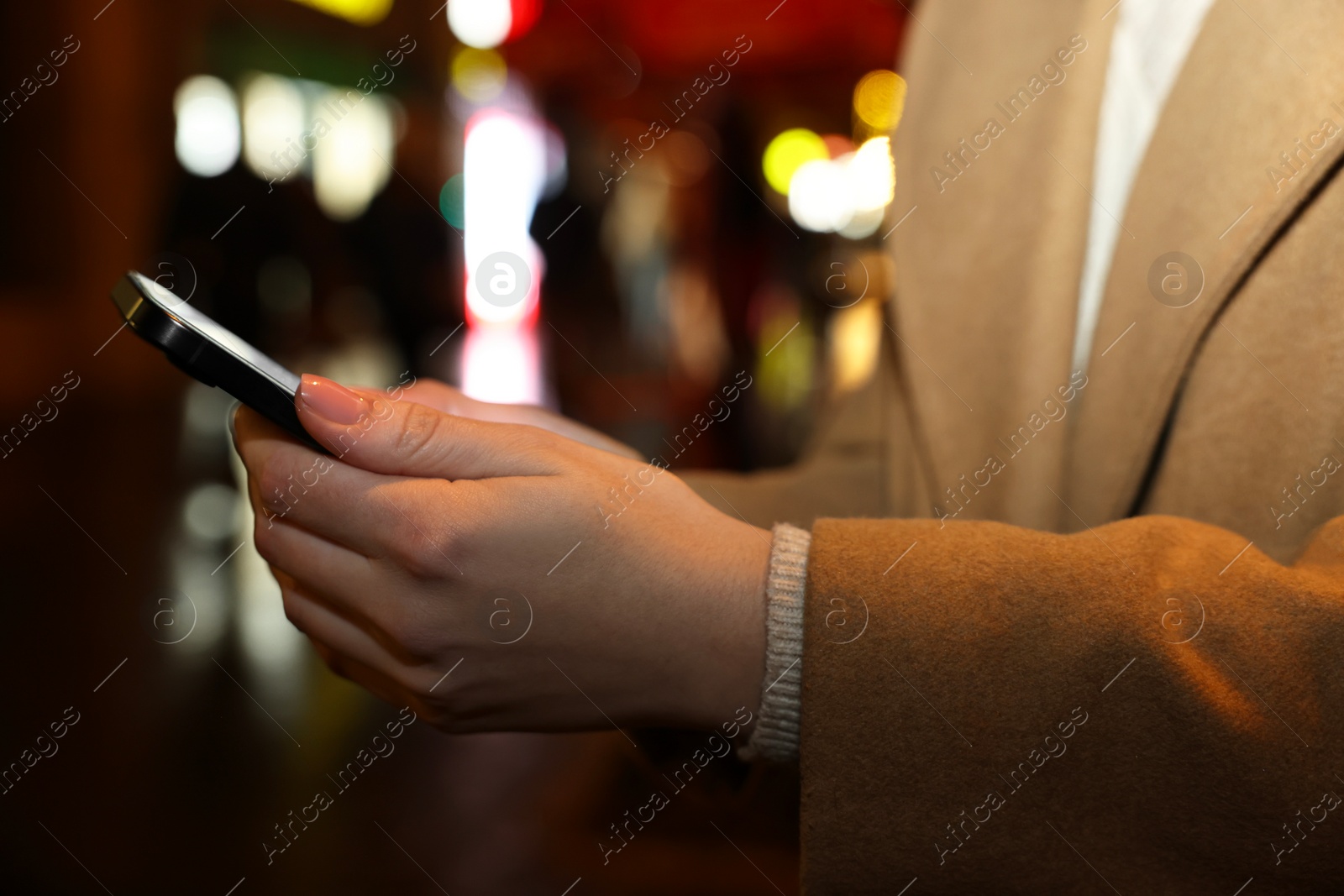 Photo of Woman with smartphone on night city street, closeup