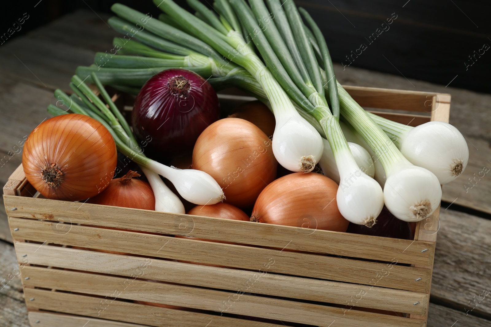 Photo of Crate with different kinds of onions on wooden table, closeup