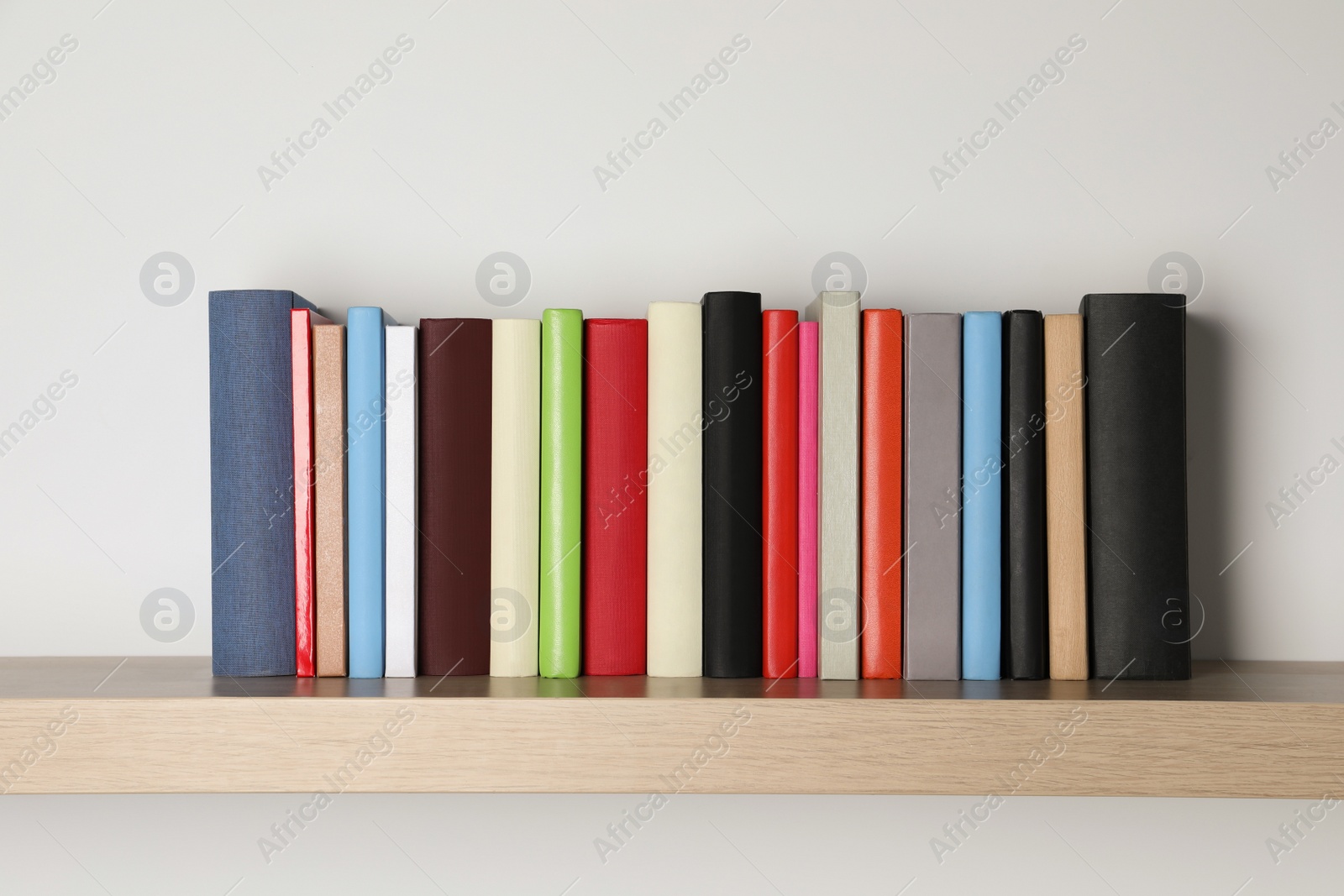 Photo of Different books on wooden shelf near white wall