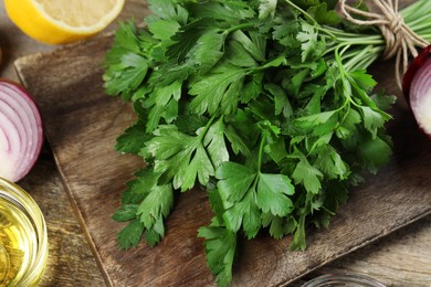 Board with fresh parsley, oil, onion and lemon on wooden table, closeup