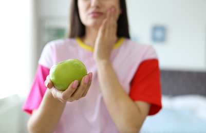 Photo of Young woman with sensitive teeth and apple at home