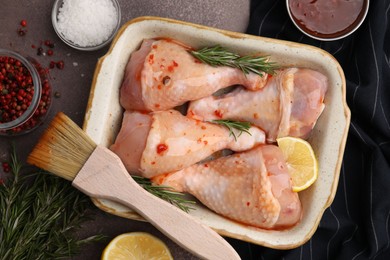 Flat lay composition with marinade and raw chicken drumsticks on brown table