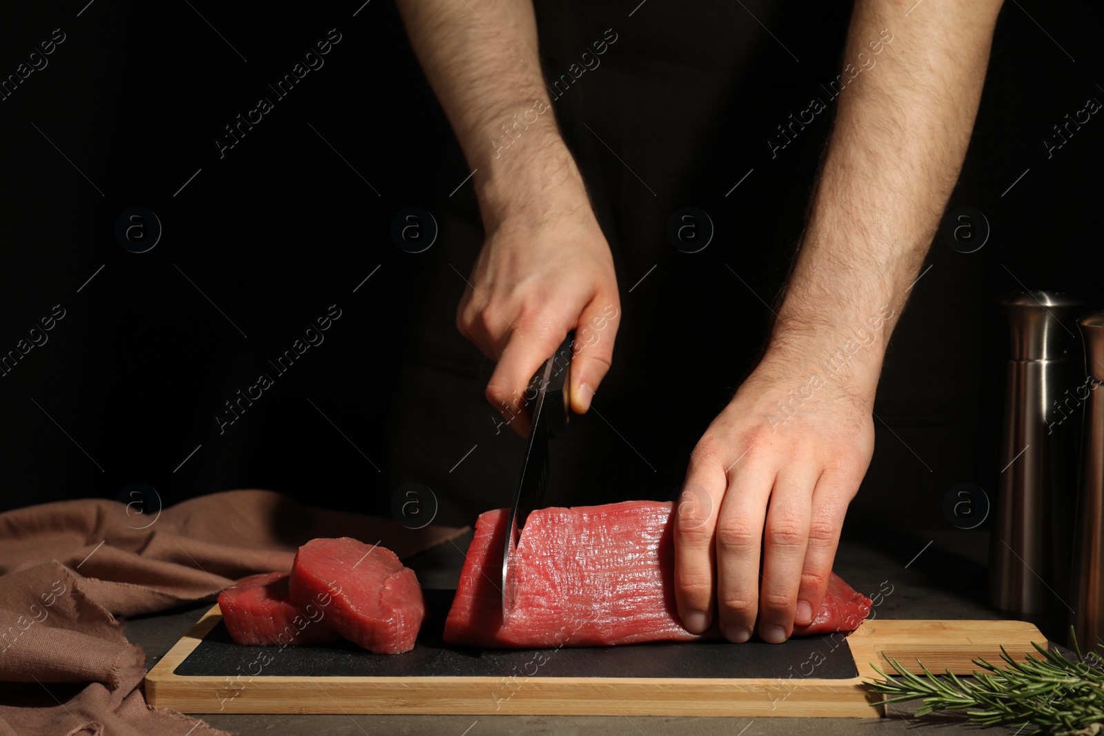 Photo of Man cutting fresh raw meat on table against dark background, closeup