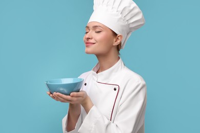 Photo of Happy chef in uniform holding bowl on light blue background