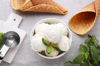 Photo of Delicious vanilla ice cream with mint, scoop and waffle cones on light grey table, flat lay
