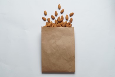 Paper bag with delicious almonds on white background, top view