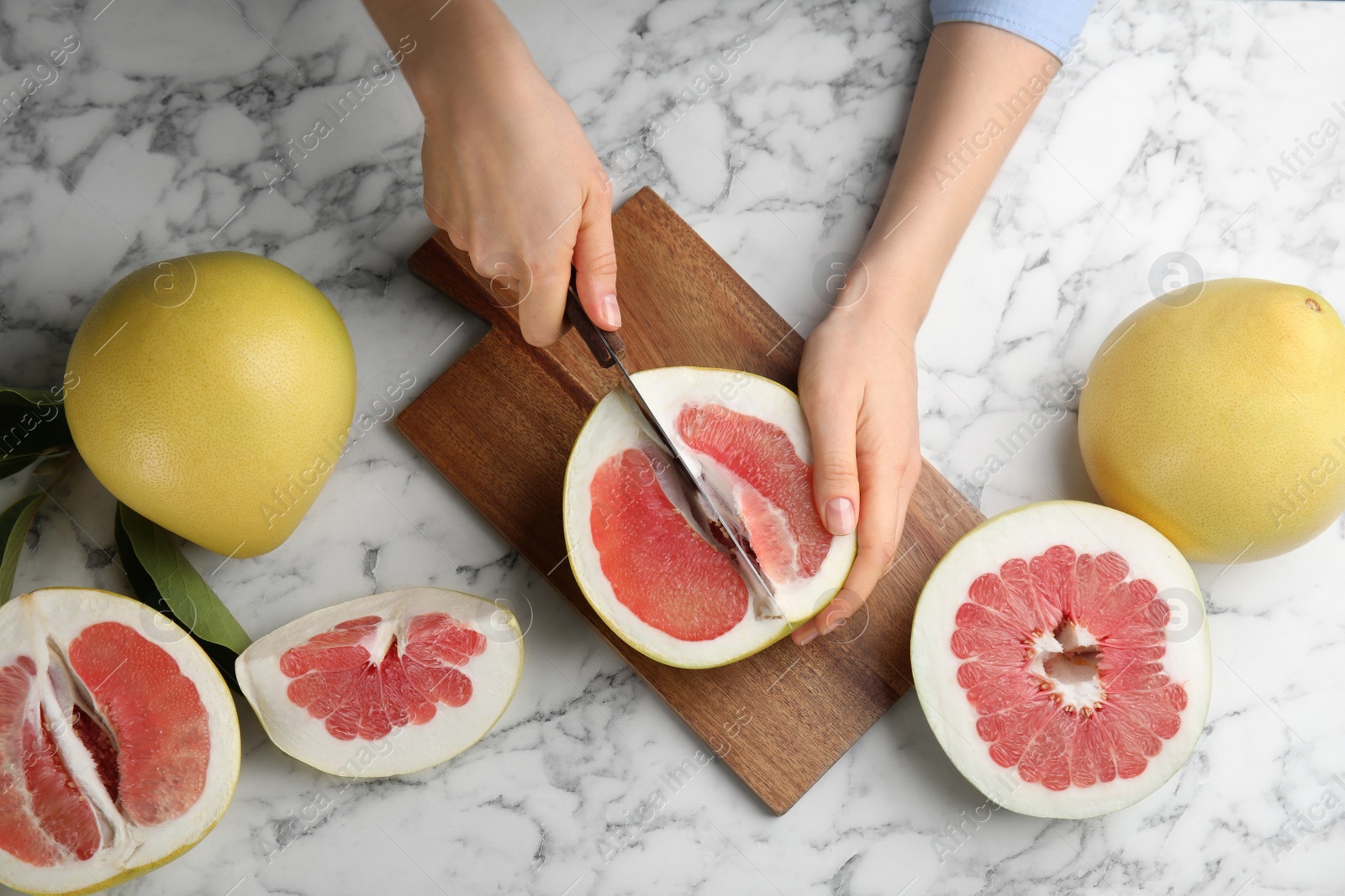 Photo of Woman cutting tasty red pomelo at white marble table, top view