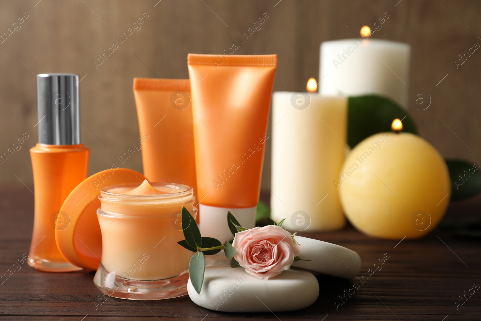 Photo of Composition with cosmetic products, spa stones and burning candles on wooden table