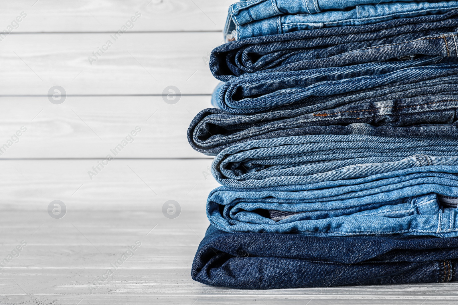 Photo of Stack of different jeans on white wooden table. Space for text