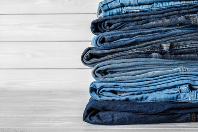 Stack of different jeans on white wooden table. Space for text