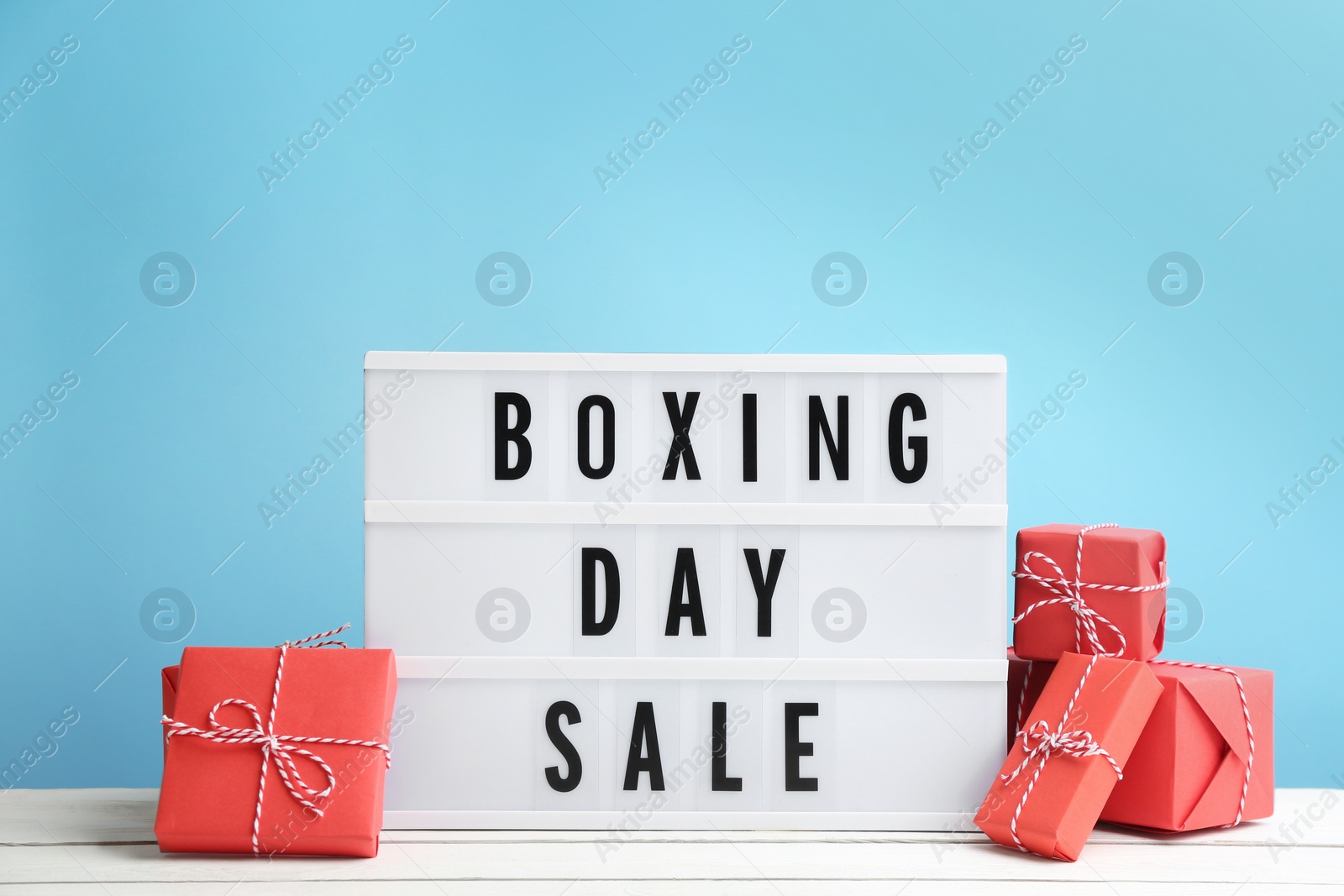 Photo of Composition with Boxing Day Sale sign and Christmas gifts on white table against light blue background