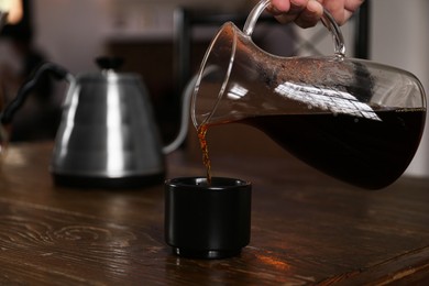 Photo of Barista pouring coffee into cup at wooden table in cafe, closeup