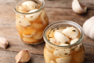 Photo of Preserved garlic in glass jar on wooden table, closeup. Space for text
