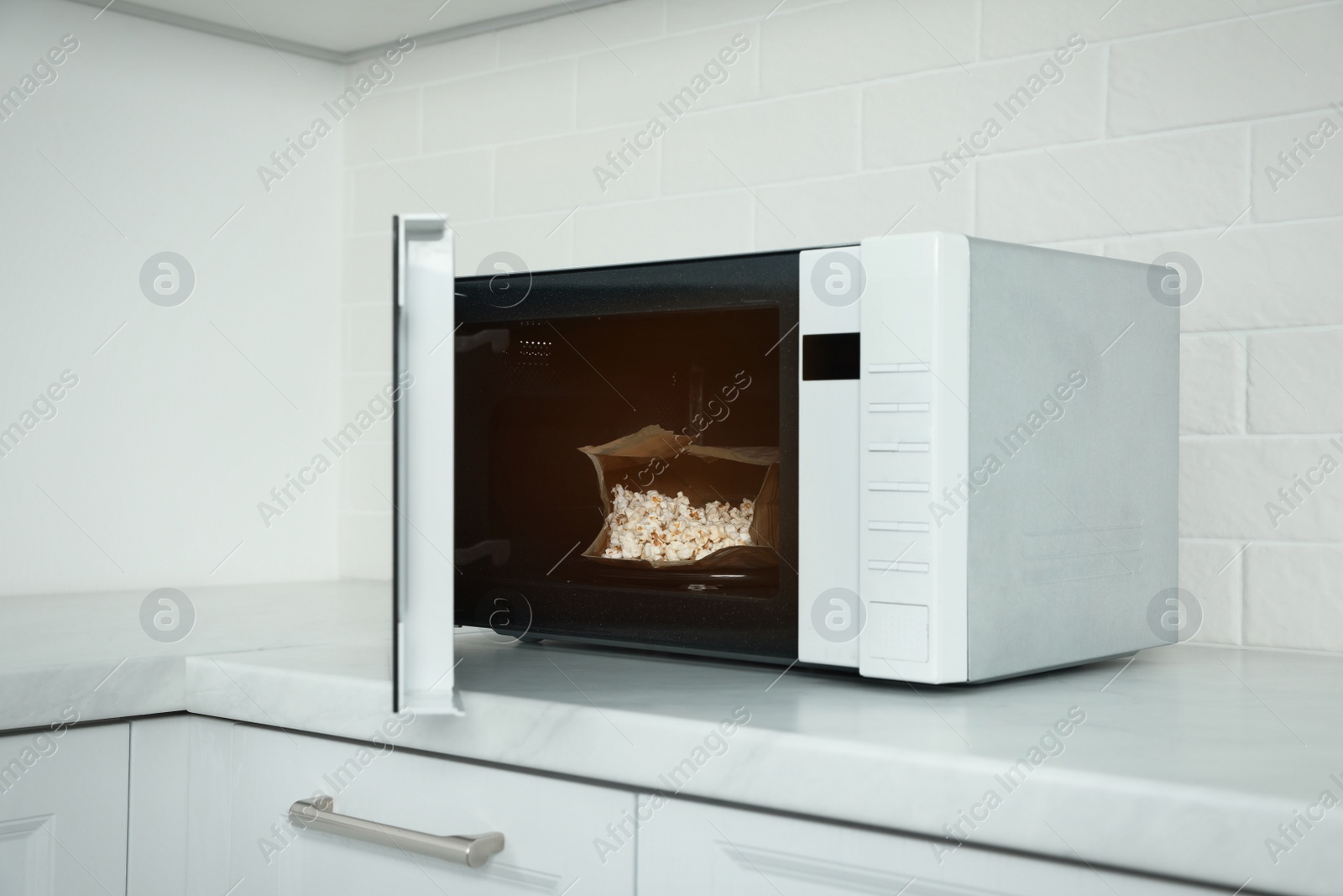 Photo of Open microwave oven with fresh popcorn on countertop in kitchen